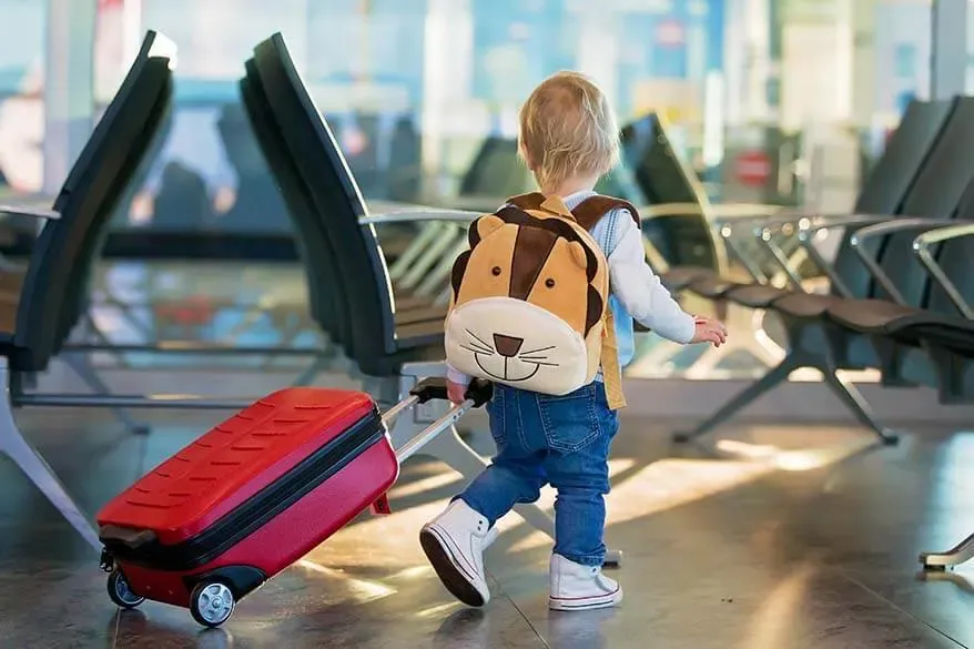 Tout-petit avec un sac à dos en forme de lion qui tire une valise rouge dans la salle d'attente d'un aéroport