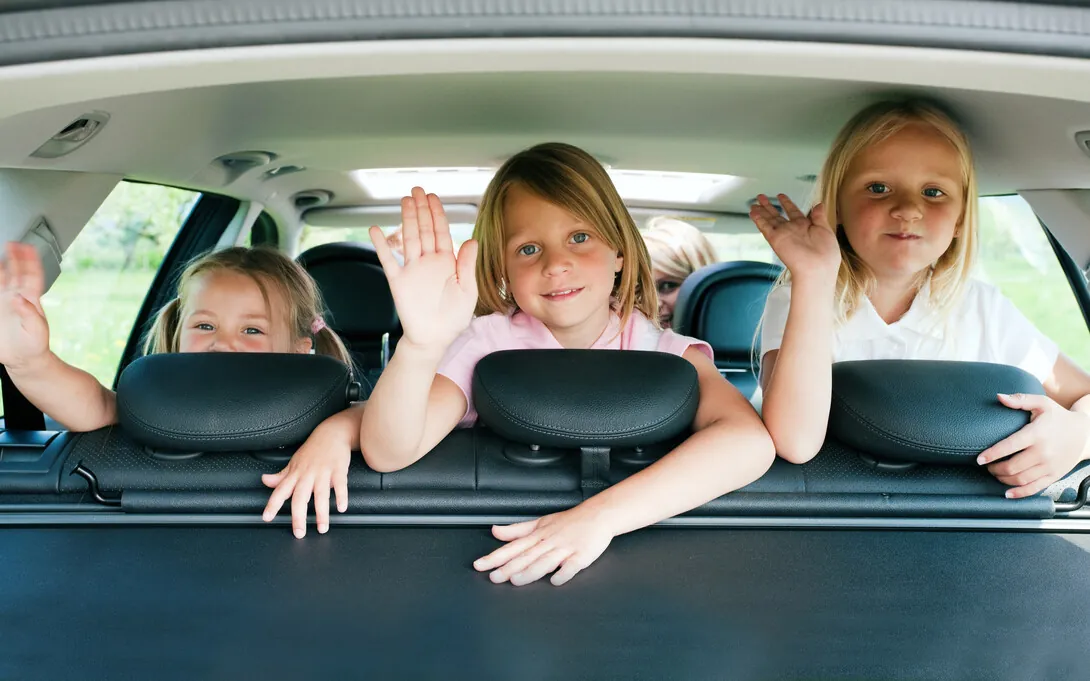 Trois enfants souriants qui saluent de la main à l'arrière d'une voiture pendant un voyage