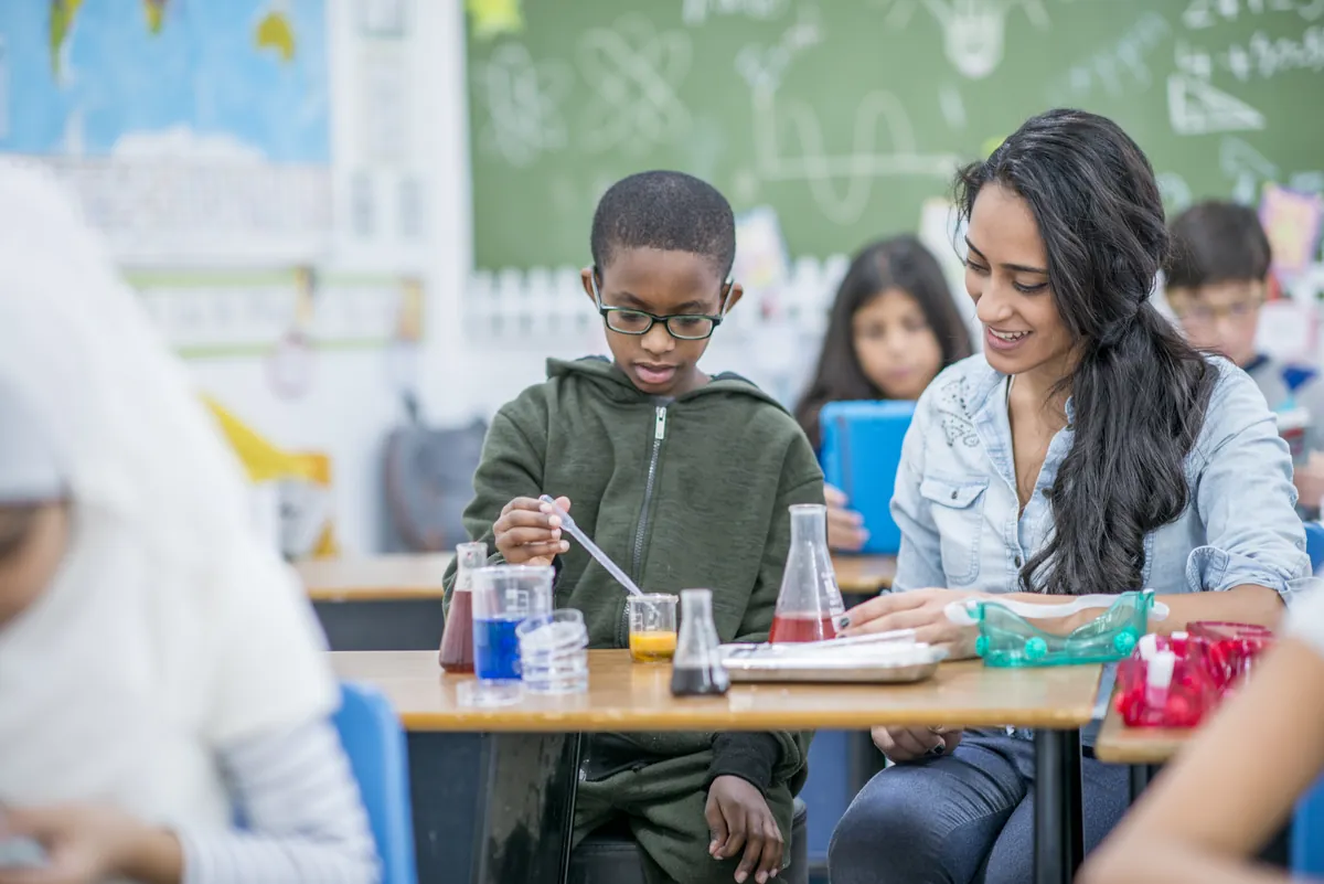 Garçon qui réalise une expérience scientifique en classe avec l'aide de son enseignante