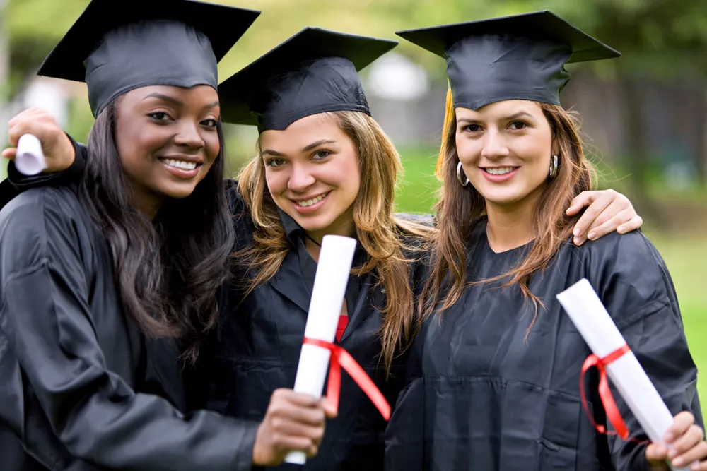 Trois finissantes souriantes en toge et mortier, diplôme en main