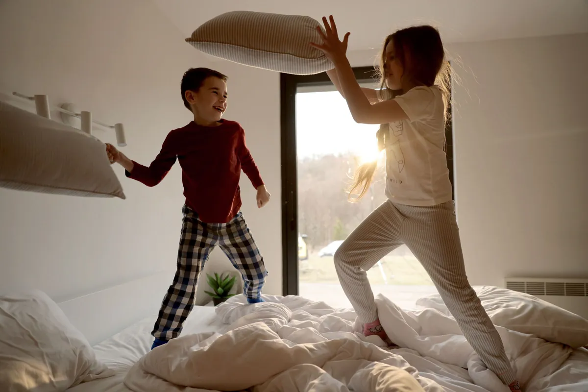Deux enfants qui sautent sur un lit en pleine bataille d'oreillers — un jeu typiquement hyperactif et impulsif