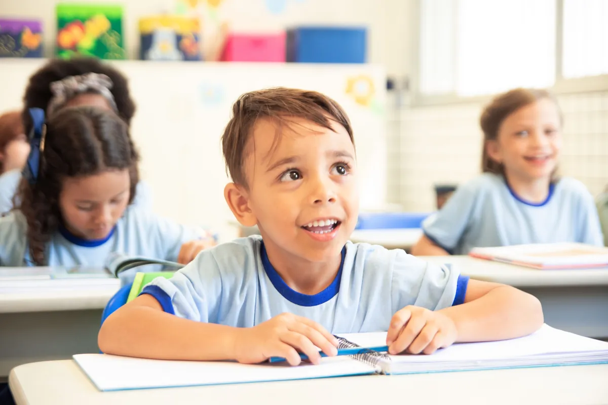 Jeune garçon souriant assis à son pupitre dans une classe lumineuse