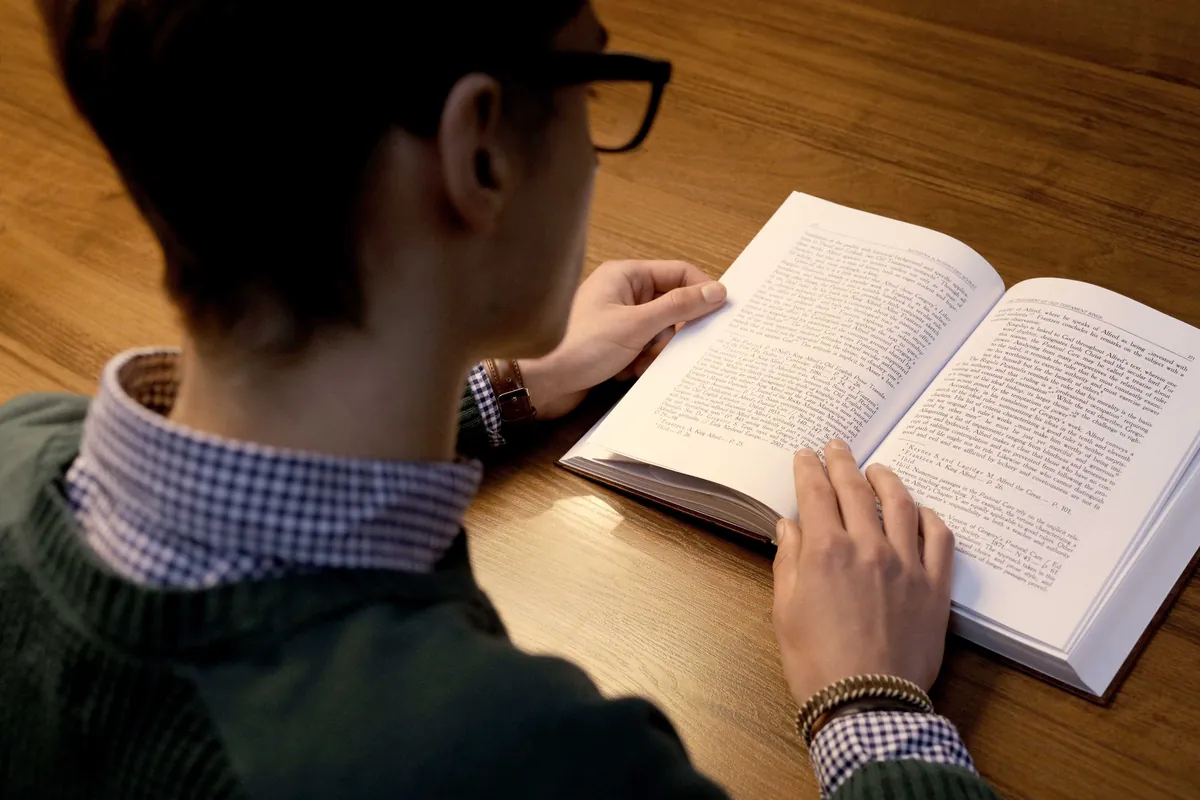 Élève qui lit un livre épais à un bureau en bois