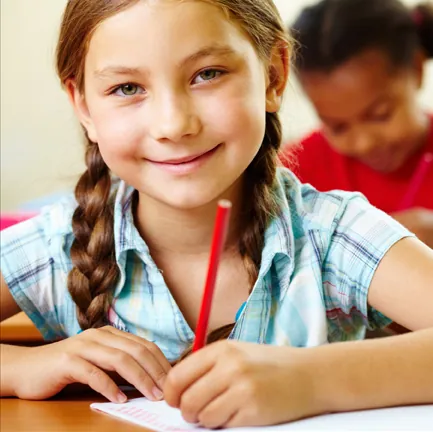 Fillette souriante qui écrit avec un crayon rouge en classe