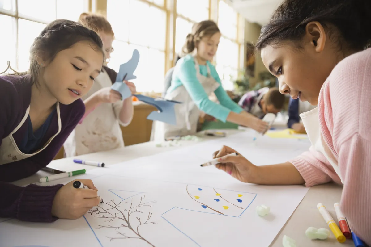 Fillettes qui dessinent et colorient ensemble sur une grande feuille en classe d'arts plastiques